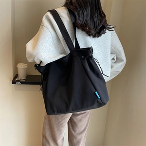 Detail of black canvas tote bag with drawstring closure and blue accent tag