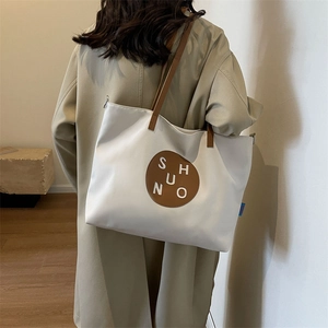 Close-up detail of white canvas tote bag featuring brown leather logo and shoulder strap