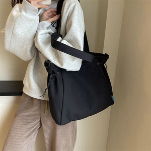 Detail of black canvas tote bag showing drawstring closure and wide shoulder strap style