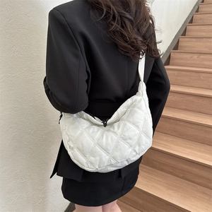 Detailed view of white quilted crescent bag with black zipper on a person