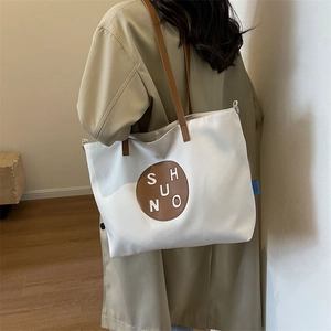 Minimalist canvas tote bag with brown leather handles worn by a model in soft indoor light