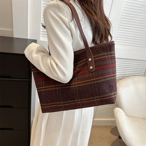 Detailed side view of dark red plaid tote bag with brown leather straps and gold rivets