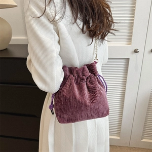 Detail of purple corduroy bucket bag with pearl strap worn by a model in a white suit
