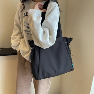 Minimalist black canvas tote bag with adjustable side drawstrings and wide shoulder strap