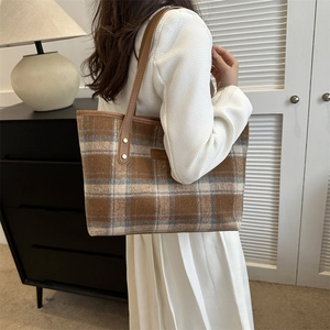 Detail of tweed tote bag with leather straps worn by model in a warm indoor setting