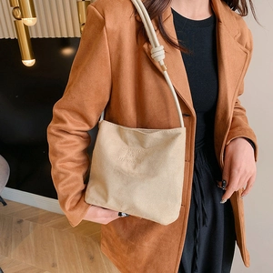 Detail of suede crossbody bag featuring onwards and upwards embossed text and knot strap
