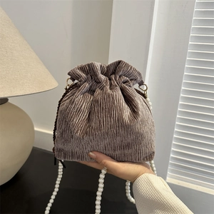 Detail of metallic pleated bucket bag with elegant white pearl decorative strap