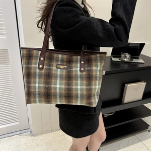 Detail of green and brown plaid tweed tote bag with leather straps and metal rivets
