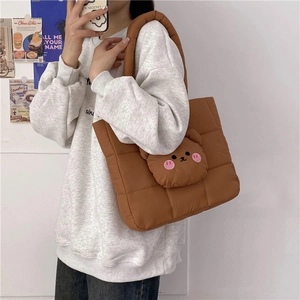 Detail of a brown quilted puffer tote bag with a 3D cartoon bear patch and square pattern