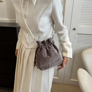 Detail of taupe pleated velvet bucket bag featuring a white pearl beaded shoulder strap