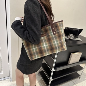 Detail of tartan wool tote bag featuring brown leather handles and a side brand patch
