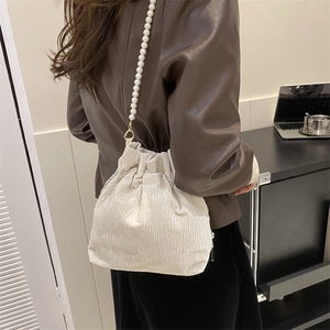 Detail of beige corduroy bucket bag with pearl chain strap worn with a brown leather jacket