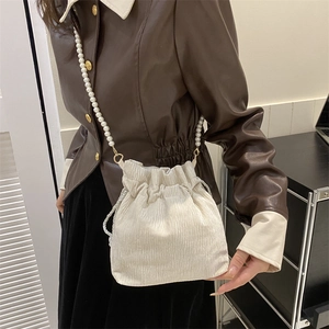 Detail of light beige velvet drawstring bucket bag with elegant faux pearl chain strap