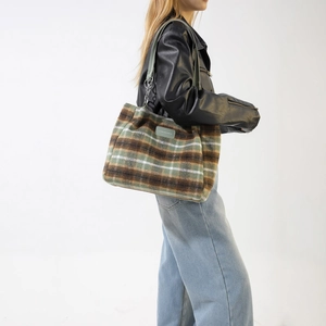 Detail of wool-blend plaid tote bag featuring a leather fashion label and metal chain strap