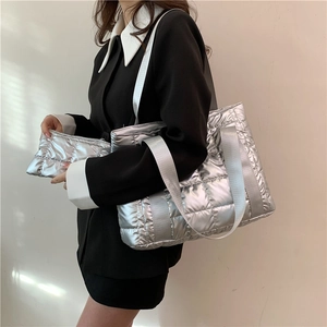 Silver quilted tote bag with metallic finish and wide shoulder strap shown on model