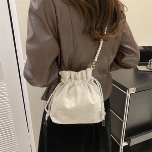 Detailed view of cream-colored pleated bucket bag with an elegant pearl chain strap