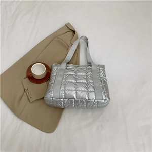 Detailed top view of silver quilted puffer tote bag on white fabric with a coffee cup