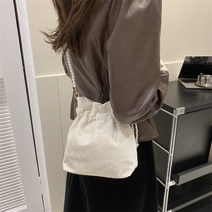 Close-up of a white pleated drawstring bucket bag featuring an elegant pearl shoulder strap