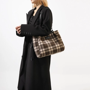 Detailed view of the brown plaid wool tote bag styled with a long black winter coat
