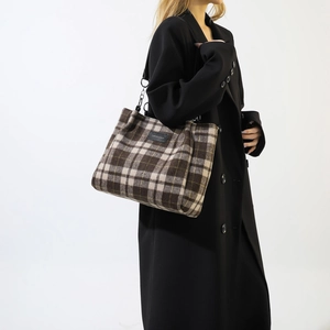 Detailed macro view of the brown plaid wool texture and black leather logo on the tote bag