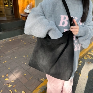 Detail of black suede tote bag showing large capacity and soft texture on female shoulder