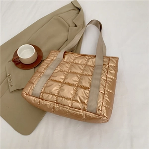 Detail of gold quilted tote bag showing padded texture and nylon handles on white surface
