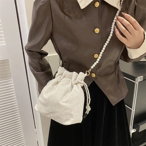 Chic cream pleated drawstring bucket bag with pearl strap worn with brown leather jacket