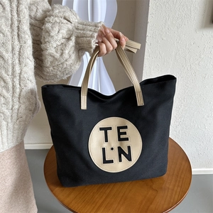 Close-up of black canvas tote bag with beige leather patch and circular logo detail