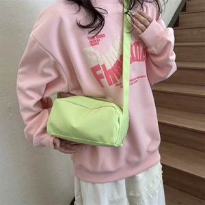 Close-up of a lime green crossbody bag with a wide strap on a pink hoodie background