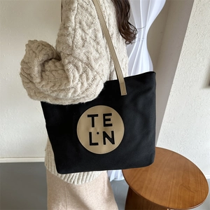 Detail of minimalist black canvas tote bag with beige shoulder straps and TE L.N logo