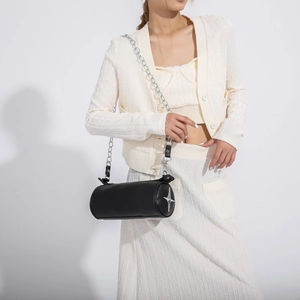 Detail of black cylindrical crossbody bag featuring silver star studs and metal chain strap