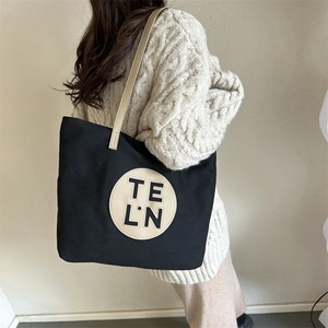 Detail view of large black canvas tote bag with slim tan straps on a knit sweater