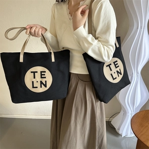 Detail showing high-quality black canvas tote bag with round leather patch and beige handles