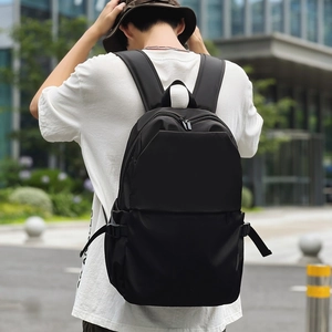 Model wearing a black nylon backpack with side buckles and zippers in a city park setting