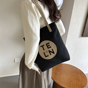 Close-up of minimalist black canvas tote bag featuring a round leather logo patch
