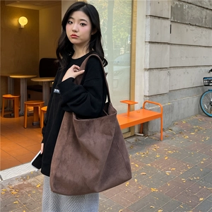 Detail of a large dark brown suede tote bag carried by a model in a street setting