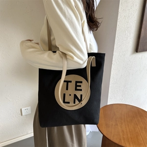 Detail of a black canvas tote bag with round logo patch and beige leather strap worn on shoulder