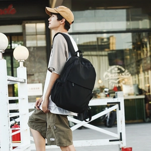 Side view of a minimalist black nylon backpack worn by a model in an urban outdoor setting