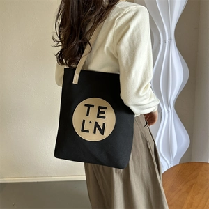 Minimalist black canvas tote bag with contrast leather straps and embossed logo patch