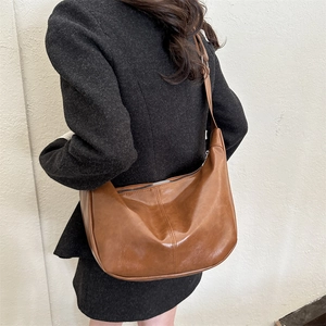 Close-up of brown PU leather hobo bag with silver zipper on model in black blazer