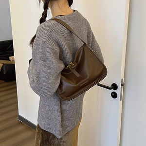 Detail of dark brown faux leather underarm bag with metal buckle on a model
