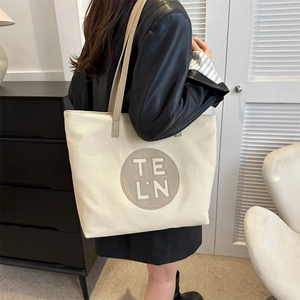 Detail of canvas tote bag with leather straps and TE LN logo shown on a person