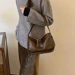 Detail of the dark brown leather shoulder bag with adjustable strap worn by a model