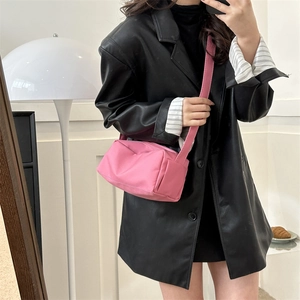 Pink minimalist nylon crossbody bag with wide strap shown on model in black leather jacket