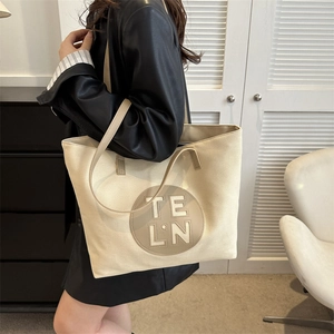 Detail of canvas tote bag featuring a leather patch with TE LN logo and shoulder strap
