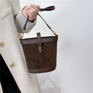 Detail of dark brown suede bucket bag featuring leather trim and gold buckle closure