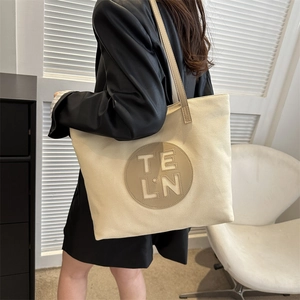 Detail view of cream canvas tote bag showing the leather logo patch and shoulder strap
