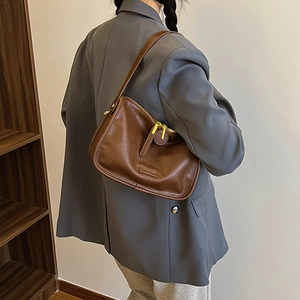 Close-up of vintage brown PU leather shoulder bag with gold hardware worn by a model