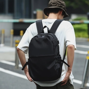 Detail of minimalist black nylon backpack with USB port shown on a model in city street