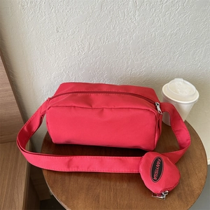 Detail of red nylon crossbody bag with mini round pouch and silver zipper on wooden stand